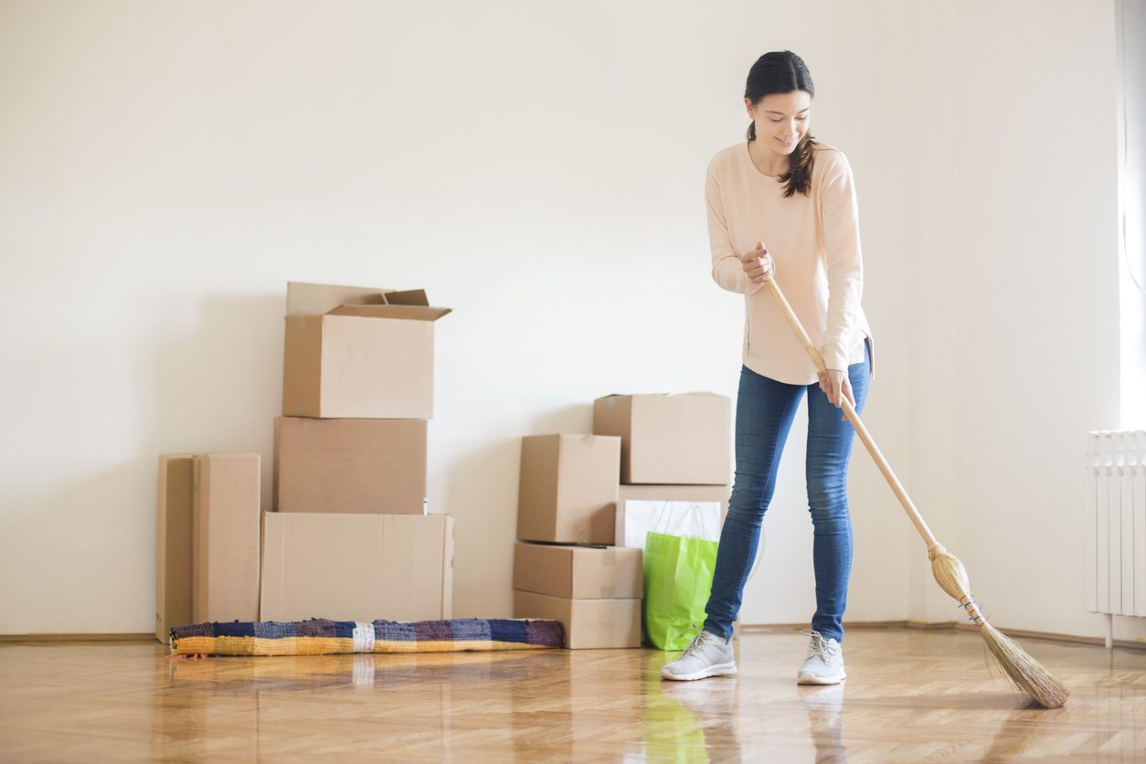 woman sweeping new home with moving boxes in the background